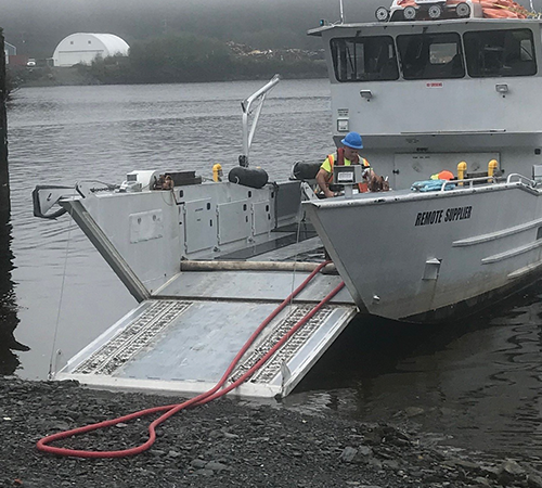 A Remote Made Easy landing craft unloading a red hose on the rocky shoreline.