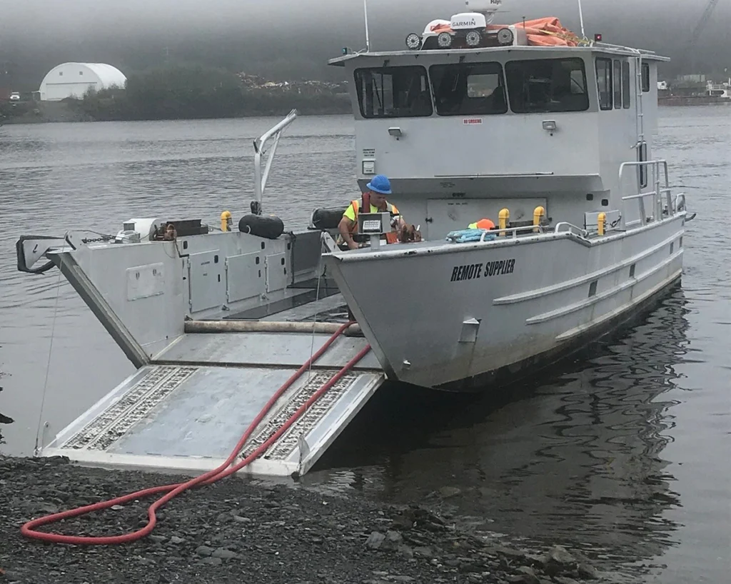 A Remote Made Easy landing craft unloading a red hose on the rocky shoreline.