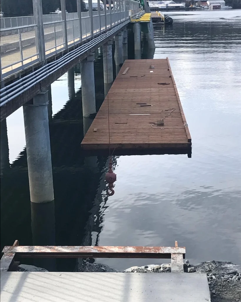Floating dock under construction alongside a pier, supported by pilings over calm water, showing marine infrastructure work in progress.